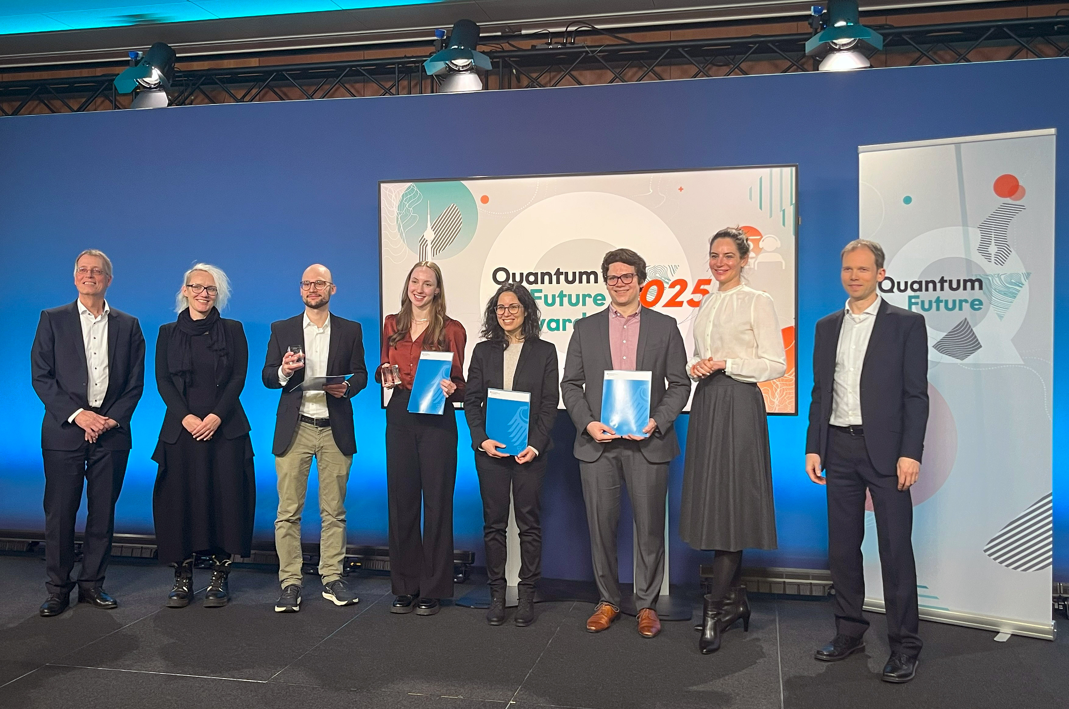 Die Preistragenden des Quantum Future Awards 2025. Dr. Marta Gilaberte Basset (4.v.r.) und Trevor Vrckovnik (3.v.r.) wurden für ihre Abschlussarbeiten auf dem Gebiet der Quantentechnologien ausgezeichnet.